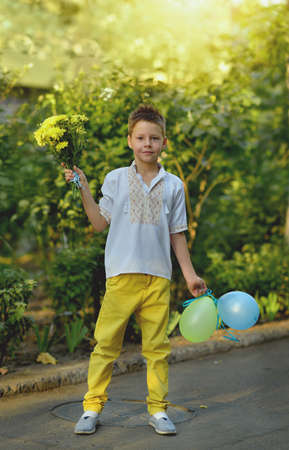 at the green bush is a cute boy in embroidery with flowers and balloonsの写真素材