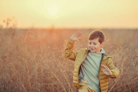 cute boy in yellow pants and jacket in the autumn field with tall grassの写真素材