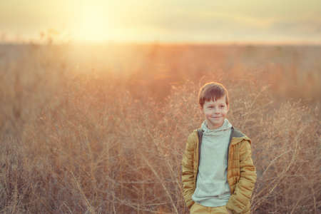 cute boy in yellow pants and jacket in the autumn field with tall grassの写真素材