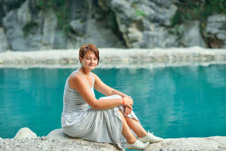 on the shores of the azure river sitting on the rocks woman in a dressの写真素材