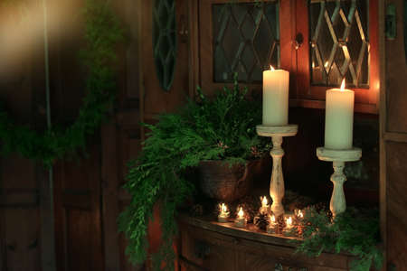 on an old cupboard burn large white candle, a vase with pine needles and cones