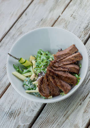 on a wooden base plate salad with barbecue meatの写真素材