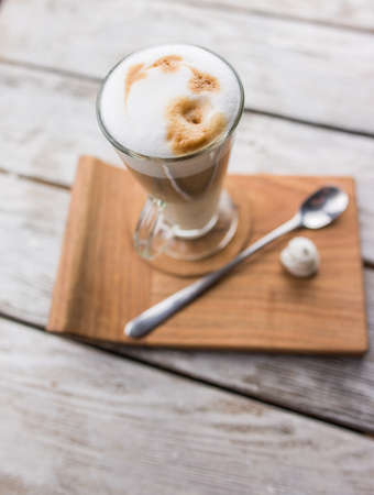 on a wooden table with a glass separation cup of latte and dessert spoonの写真素材