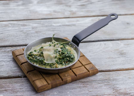 pan with spinach and cream sauce and parmesan cheese on a wooden boardの写真素材