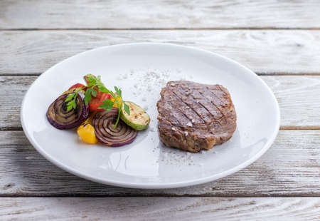 on the wooden table white plate with steak and grilled vegetablesの写真素材