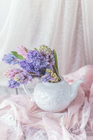 White teapot with a large bouquet of multicolored hyacinths and a cup on a pink openworkの写真素材