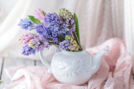 White teapot with a large bouquet of multicolored hyacinths and a cup on a pink openworkの写真素材