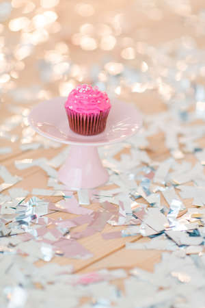 shiny confetti on the table and a plate with pink cupcakesの写真素材