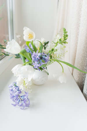 sunny day on the windowsill is a white vase with a bouquet of flowers from tulips and hyacinthの写真素材