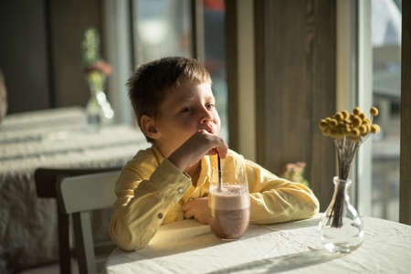 in a cafe boy in a yellow shirt cocoa drinks through a strawの写真素材