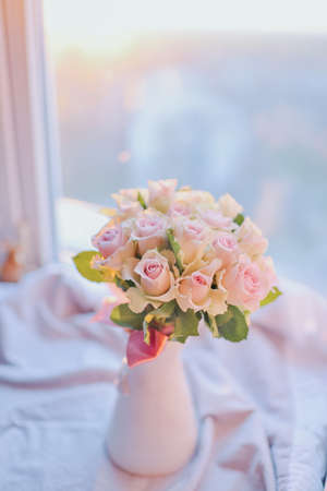 at sunset at the window in a pink vase bouquet of roses with bowの写真素材