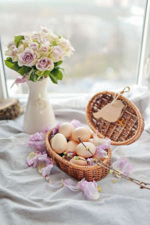 window wicker basket with eggs and a vase with a bouquet of roses