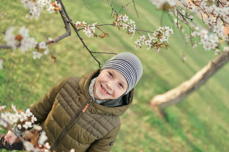 boy in a jacket and hat walking in the garden with flowering treesの写真素材