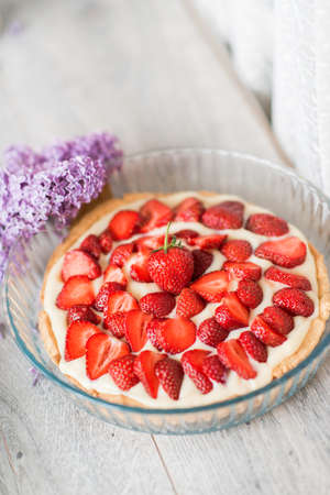 on a light background a bouquet of lilac in a white vase and a large cake with strawberriesの写真素材