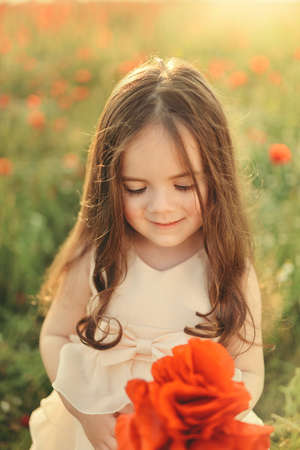 the sun on the field little girl with long hair with a bouquet of red poppiesの写真素材