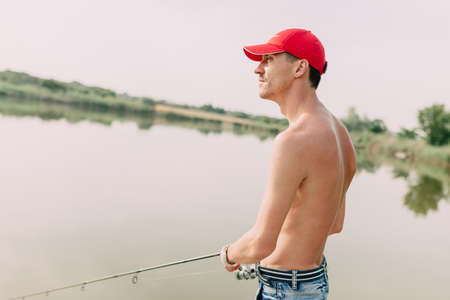 warm sunny day a guy in a red cap at the lake catches fishの写真素材