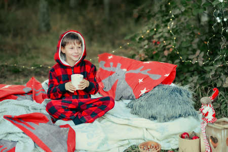 in the woods on the bed sits a boy in a red suit with a cup