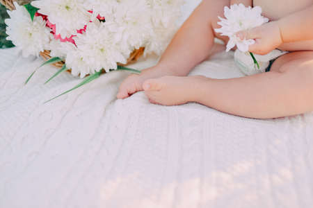little baby on the bed legs and a bouquet of white flowersの写真素材