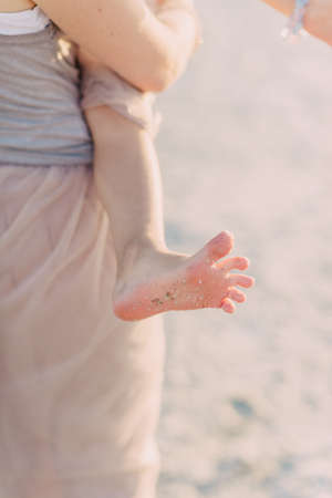 on the beach at mum on hands of the baby and children's foot barefoot in the sandの写真素材