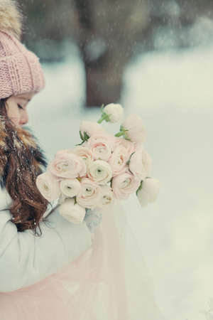 in the forest of snow in winter beautiful girl with long hair in a hat and a bouquet of rosesの写真素材