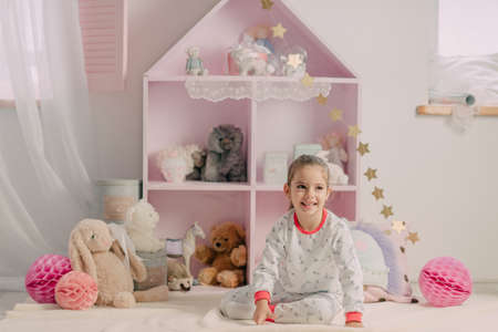 in the nursery pink home closet with toys, a cheerful girl in pajamasの写真素材