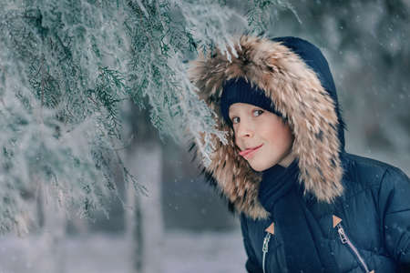 boy in a jacket with a hood with fur walks snow park with trees in the snowの写真素材