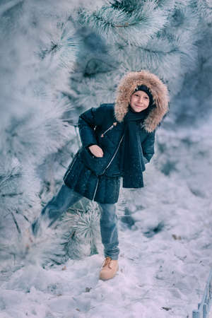 boy in a jacket with a hood with fur walks snow park with trees in the snowの写真素材