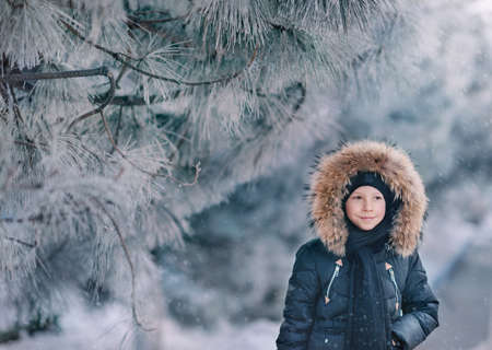 boy in a jacket with a hood with fur walks snow park with trees in the snowの写真素材