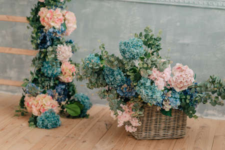 On the wooden floor a beautiful bouquet of hydrangeas in a large wicker basket and flower garland.の写真素材