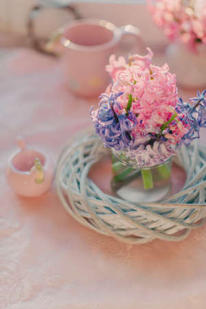 On the table there is a bouquet of a pink hyacinth in a glass vase with a wreath and a pink cup of a chickenの写真素材