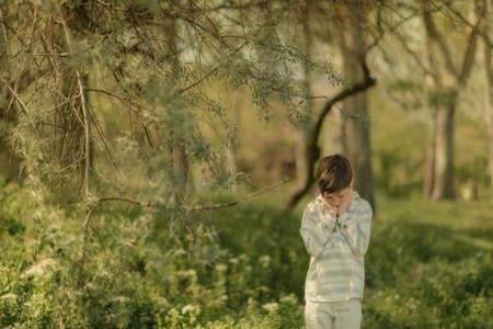 In a sunny forest, a little boy in white jeans and a striped cardigan walkの写真素材