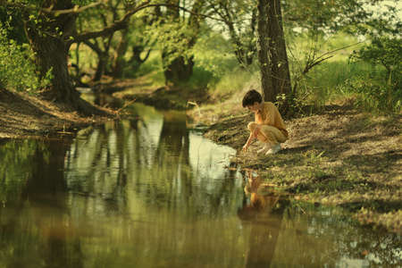 A sunny afternoon in the park by the river walks a small boy with jeans and cardiganの写真素材