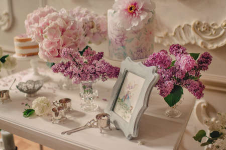 On white table vases with lilac and hydrangea, cake and picture in frame