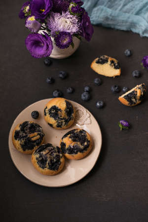 a plate of cakes with blueberries on a decorated table on which stands a vase of flowersの写真素材