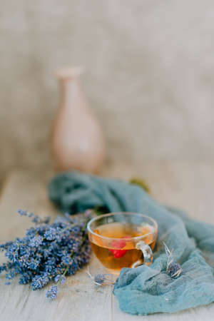 glass cup of tea with raspberries on the background of a bouquet of lavender wrapped in a scarf