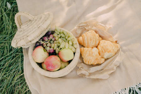 on a glade a wicker basket with grapes and apples next to croissantsの写真素材
