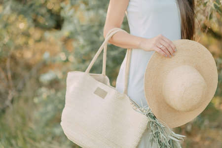 girl with a hat in her hand holding a straw bag with a sprig of oliveの写真素材