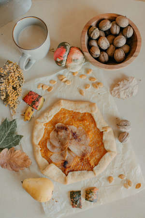 Pumpkin pie with a pear on a decorated table with a wooden plate of nutsの写真素材