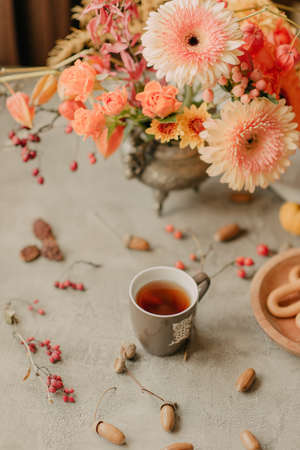 On the table an old vase with various flowers, a cup of tea and a plate of bagelsの写真素材