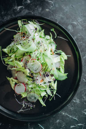 fresh salad of vegetables and microgreens on a black plateの写真素材