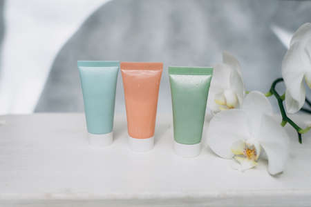 Set of cosmetic bottles with cream, lotion, shampoo, conditioner and orchid flowers on white wooden backgroundの写真素材