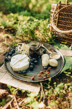 Camembert cheese with blueberries and honey in a glass jar on a wooden board in the forest.の写真素材