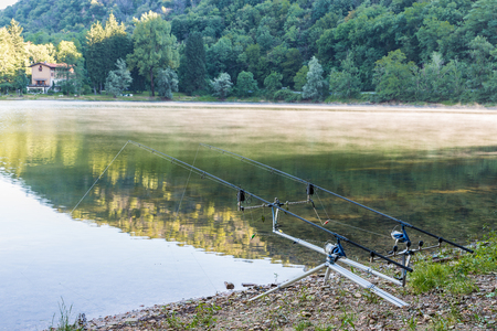 Fishing adventures. Carp rods propped on a rod pod with two bite alarms, as a background a lake with low mistの写真素材