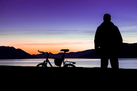 Mountain bike and biker. Silhouette of a mountain bike and of a cyclist who is watching the sunset over the lake (lake Maggiore - Maccagno, Italy) - Focus on mountain bikeの写真素材
