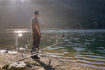 Fishing adventures, carp fishing. Angler on the shore of a lakeの写真素材