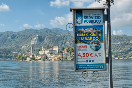 Orta San Giulio, Italy â October 9, 2018: Lakefront of the picturesque village on Lake Orta. Sign that advertises the sightseeing tour on the island of San Giulio on background. Focus on the billboardのeditorial素材