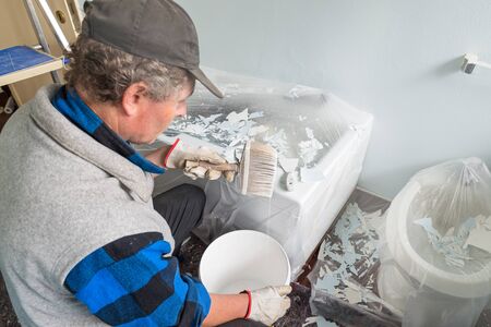House painter with dripping brush in hand. Home renovation concept. Bathroom painting work,...