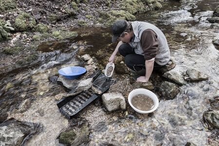 Outdoor adventures on river. Gold panning, man pours sand and gravel into a sluice box in search of goldの写真素材