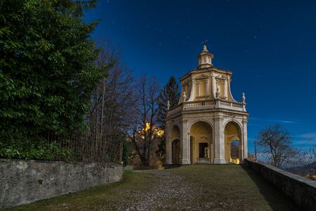 Sacred way in the moonlight. Sacro Monte di Varese, Italy,   with the thirteenth chapel and the village of Sacro Monte illuminated on the left in the distanceの写真素材
