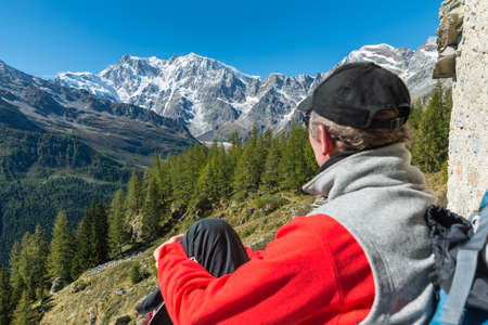 Italian Alps and hiker resting while admiring the view. In the background the Monte Rosa with its glacier. Macugnaga, Italy. Concept of hiking, sports and outdoor activities. Focusの写真素材